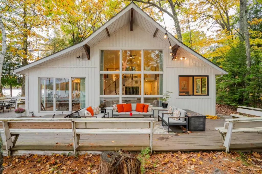 White cabin with large grid windows and a patio furniture setup on the wooden deck