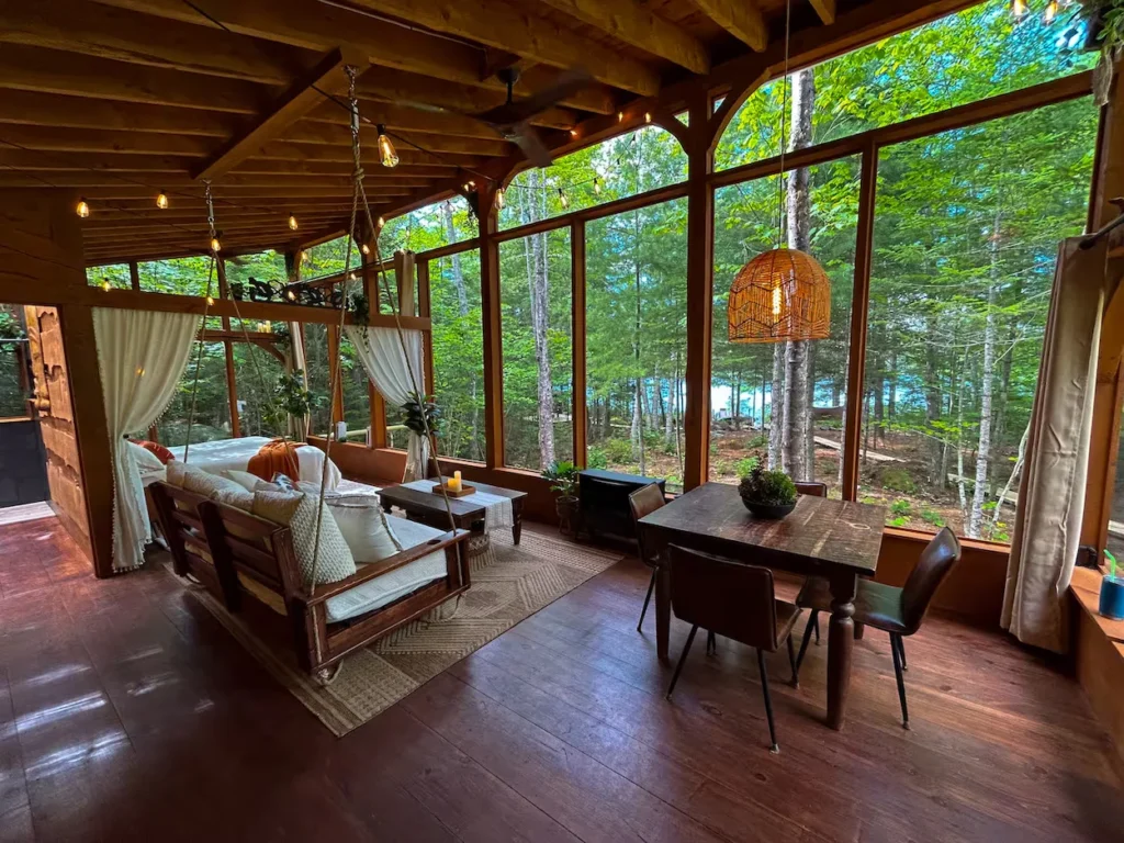 Screened porch with a hanging daybed, dining table, and lake views