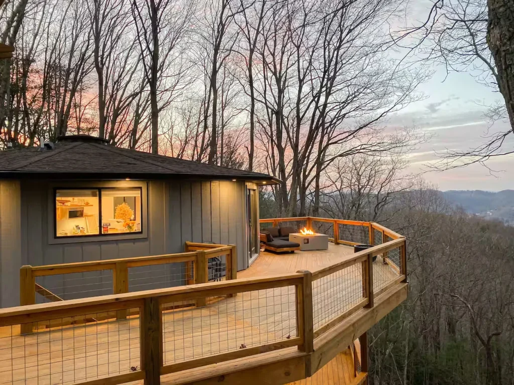 Round wooden cabin with a large wraparound deck, outdoor fire pit, and sunset mountain views