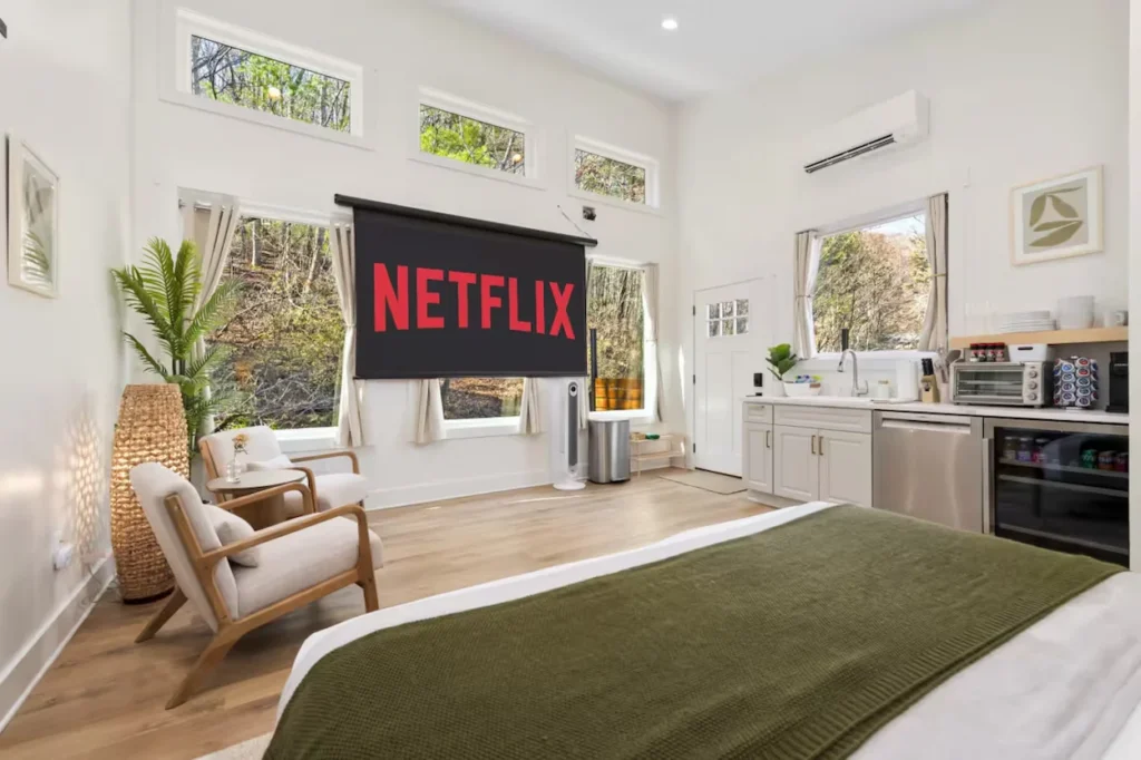 Studio cabin interior with a bed, armchairs, kitchenette, and pulled-down movie projector screen