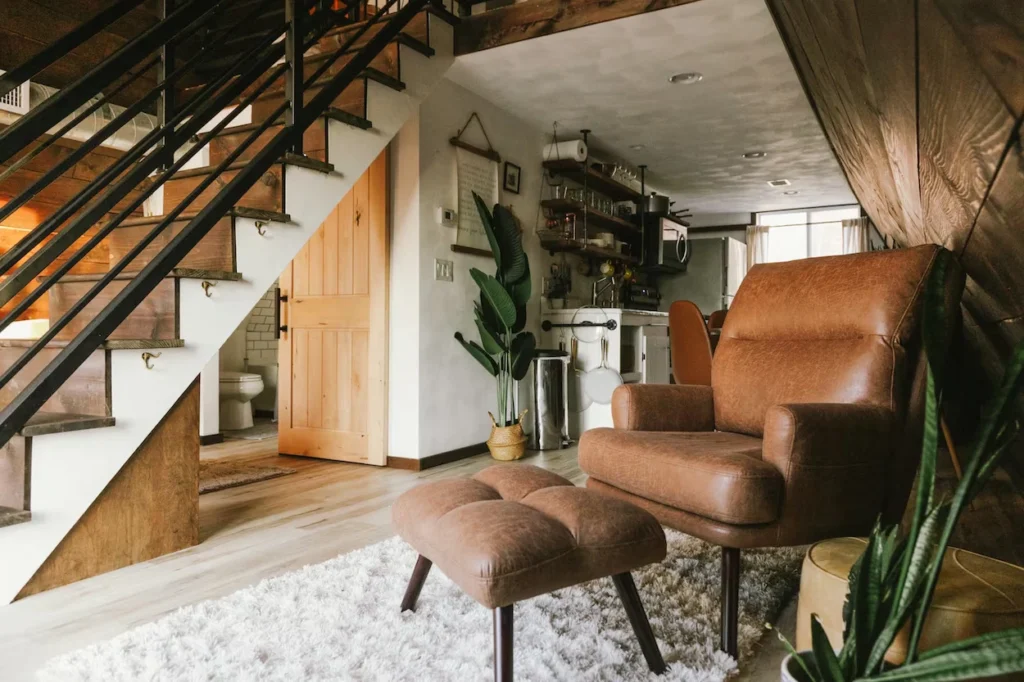 Brown leather armchair and ottoman on a shag rug under floating cabin stairs
