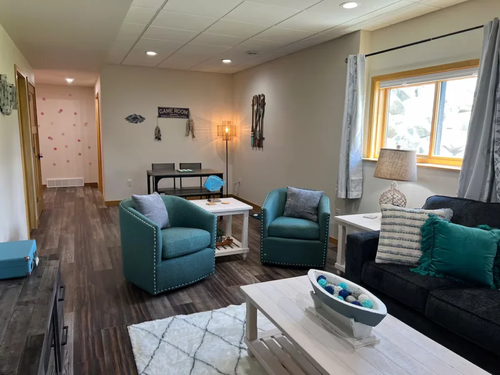 Basement living room featuring two teal swivel chairs, a dark sofa, and a white coffee table