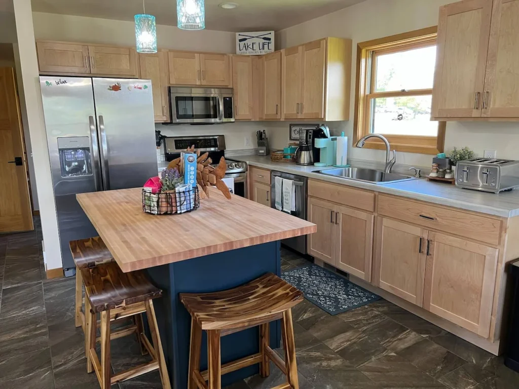 Lake house kitchen featuring light wood cabinets, a blue central island with wood stools, and stainless steel appliances