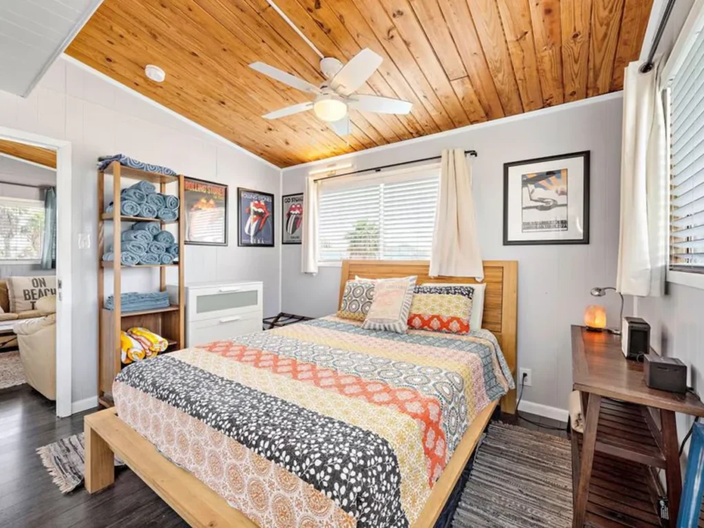 Cozy beach house bedroom with a light wood bed frame, patterned quilt, and wood-paneled ceiling