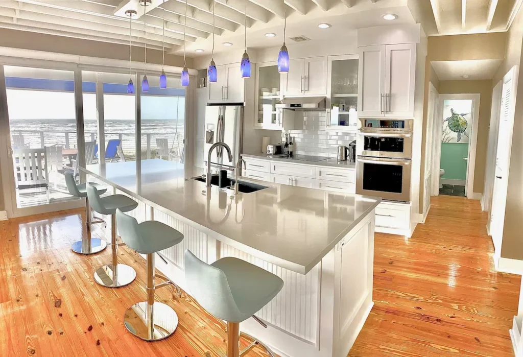 White beach house kitchen with a large island, blue pendant lights, and ocean views