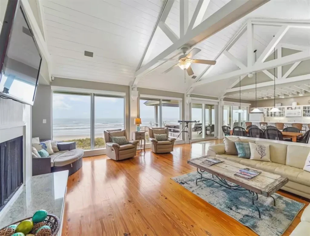 Beach house living room with vaulted white ceilings, hardwood floors, and panoramic ocean views