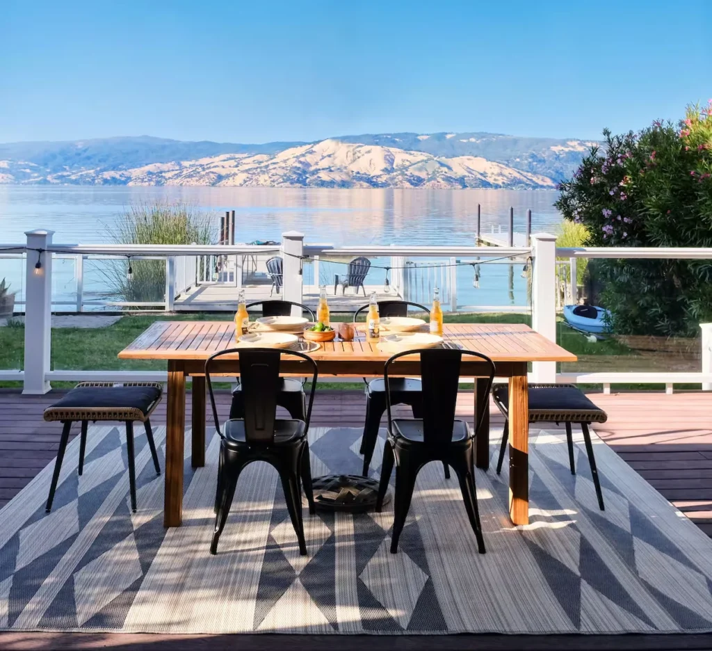 Outdoor dining table and chairs set on a wooden deck overlooking Clear Lake and mountains in California