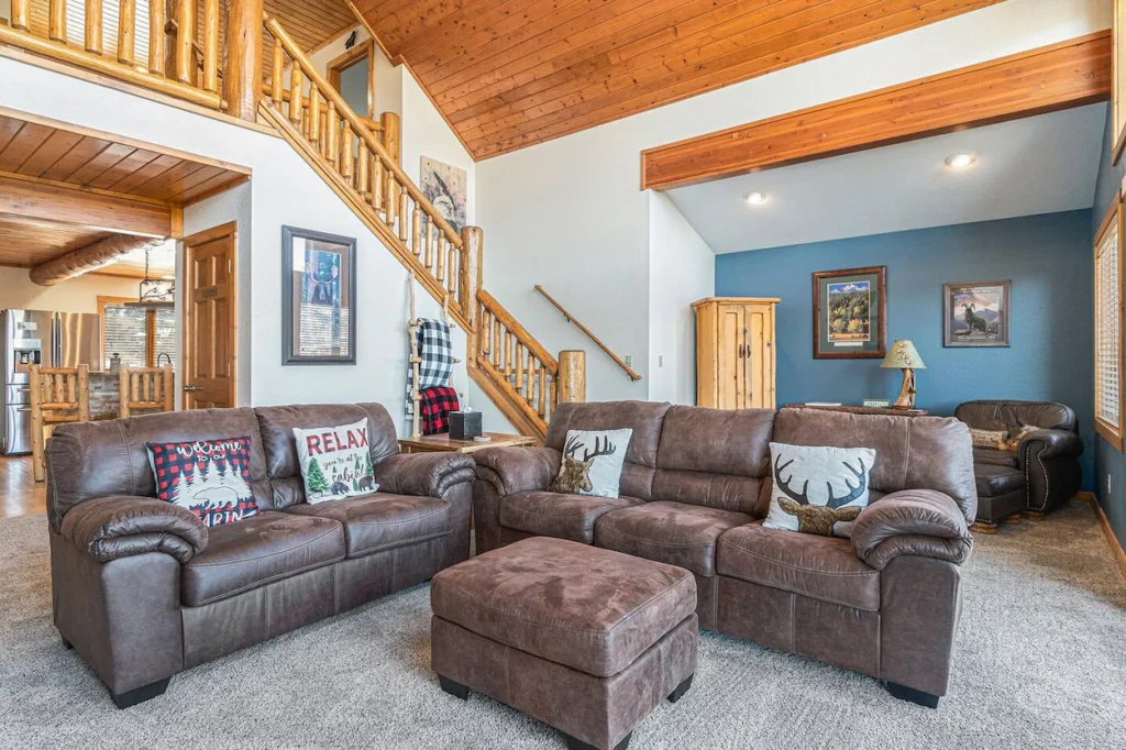 Log cabin living room featuring brown leather sofas, an ottoman, and a wooden staircase