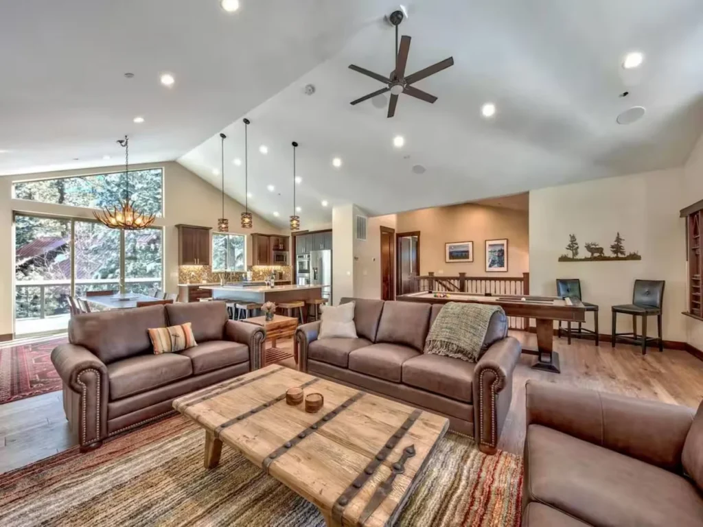 Spacious mountain cabin living room with leather sofas, a rustic wooden coffee table, a kitchen island, and a pool table