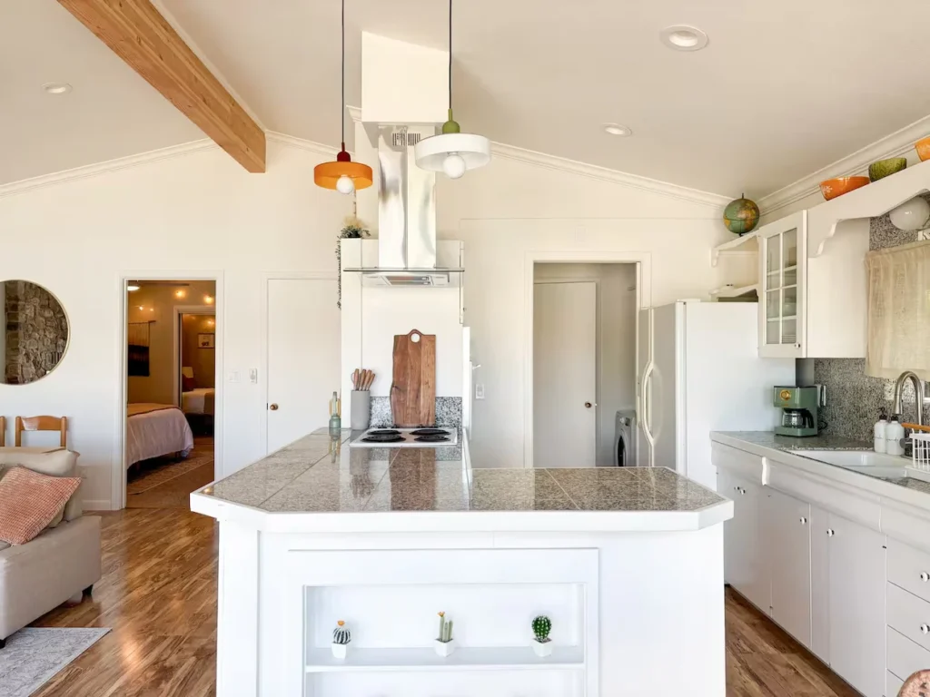Bright midcentury modern kitchen with a white central island, granite countertops, and colorful pendant lights