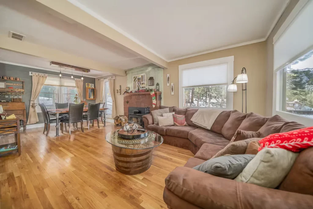 Open-concept cabin living room with a large brown sectional sofa, barrel coffee table, and dining set