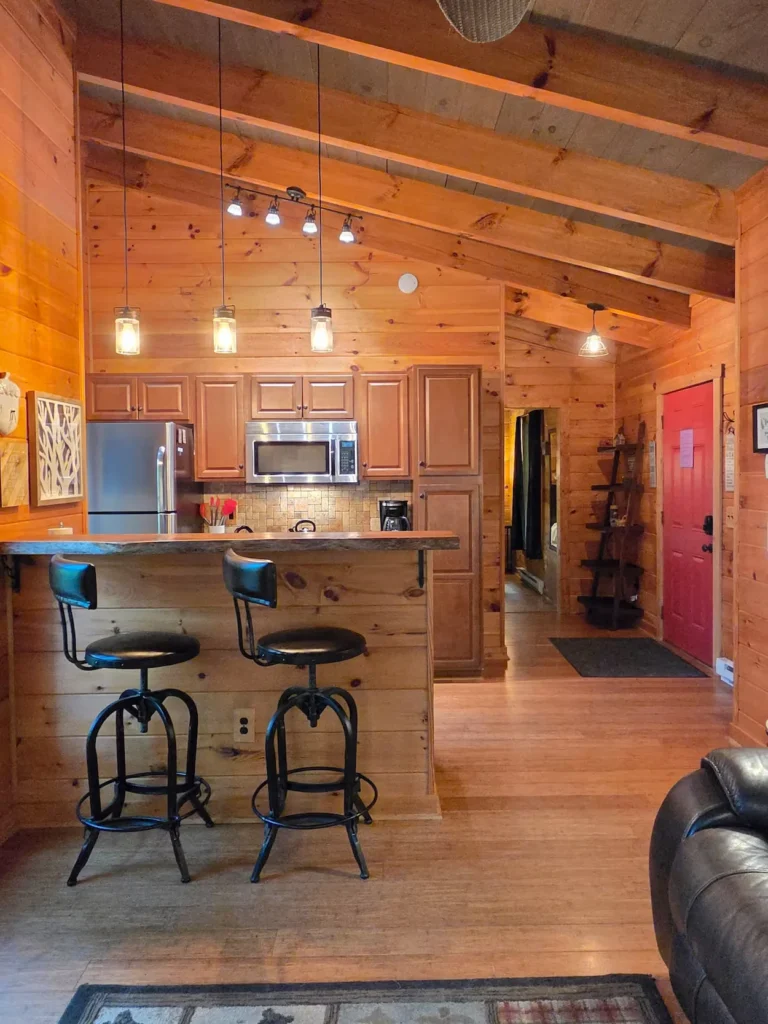 Wood panel kitchen with a breakfast bar, two black stools, and a bright red front door