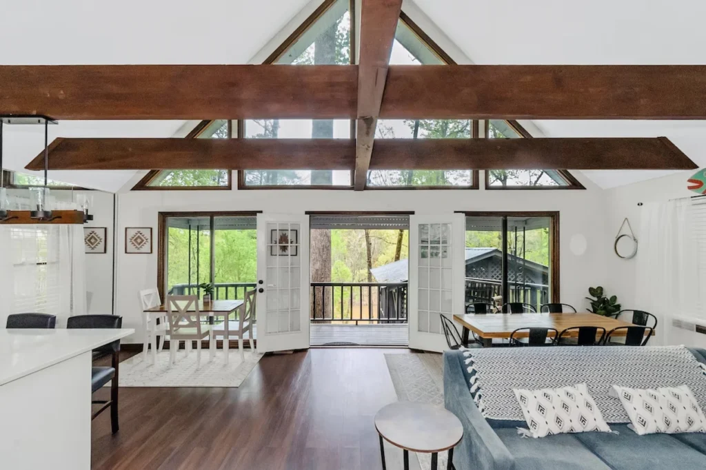 Open cabin interior with exposed wood beams, double dining tables, and large windows