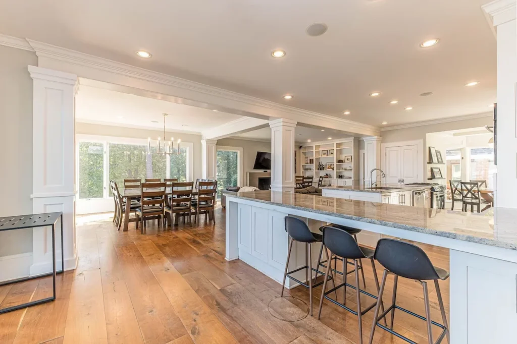Bright lake house kitchen with black barstools, granite breakfast bar, and a large wooden dining table