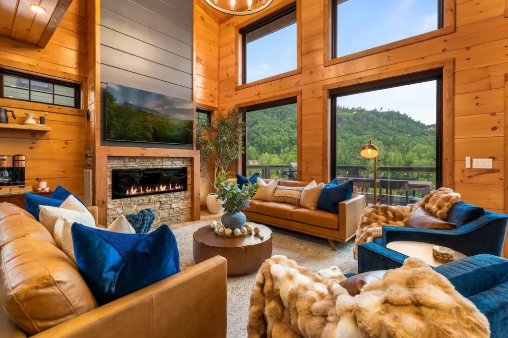 Modern cabin living room with leather couches, fireplace, and large mountain-view windows