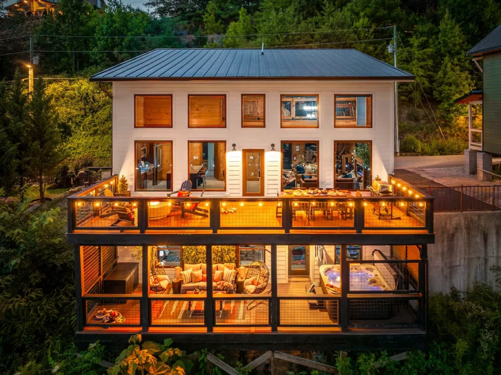 Two-story illuminated modern cabin with a hot tub and string lights on the deck