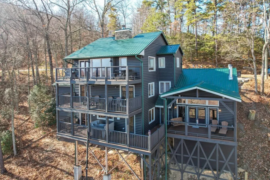 Large dark gray three-story cabin with a green metal roof and multiple decks