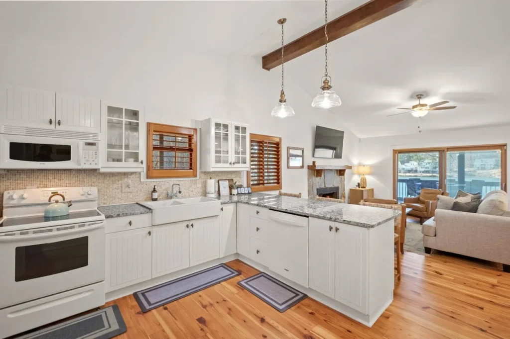 Bright cabin kitchen with white beadboard cabinets, granite countertops, and open view to the living area