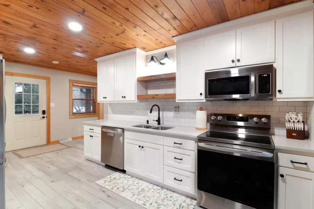 Modern kitchen with white cabinets, stainless steel appliances, and a wood ceiling