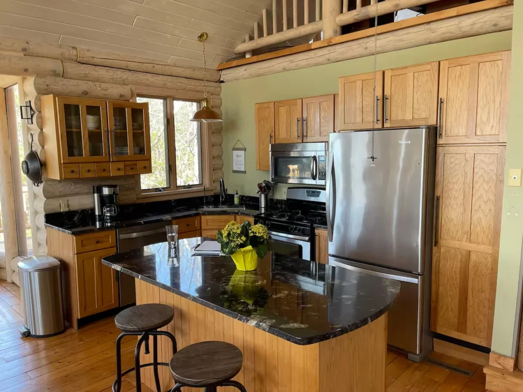 Log cabin kitchen with oak cabinets, a dark granite island, and stainless steel refrigerator
