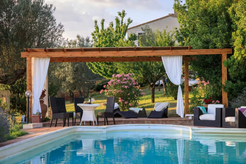 Private swimming pool and a wooden pergola with white curtains and patio furniture at an estate in Guardea