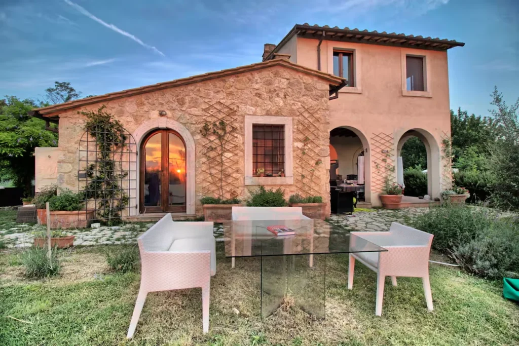 Stone country villa featuring arched entryways and a glass dining table on a green lawn