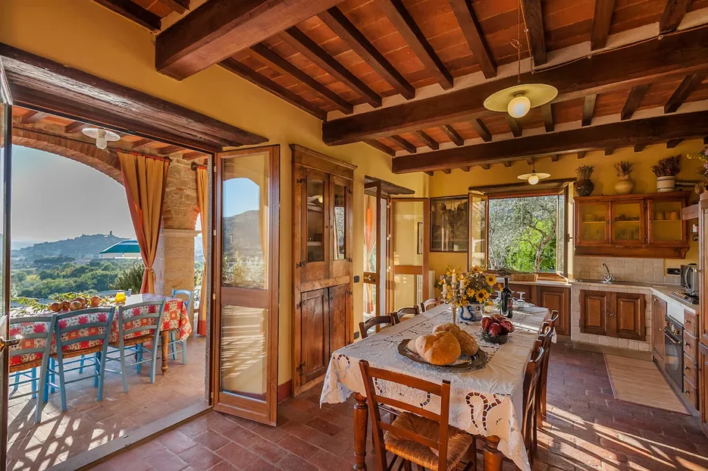 Rustic Tuscan kitchen and dining table with exposed wood ceiling beams opening to an outdoor patio