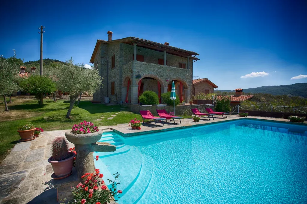 Stone exterior of Villa Senaia in Tuscany with pink lounge chairs next to a large swimming pool