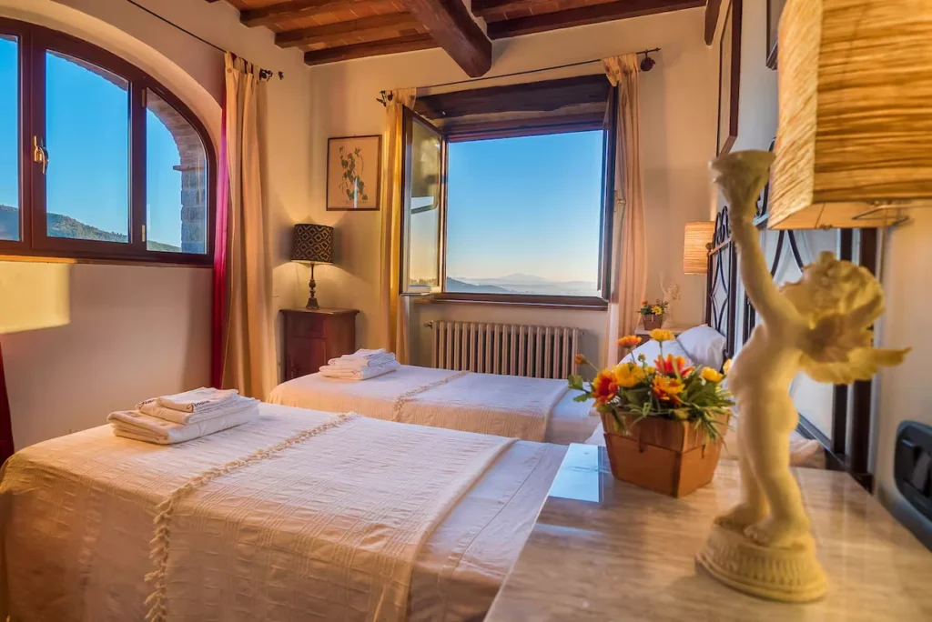 Tuscan bedroom with two twin beds and an open window overlooking distant mountains