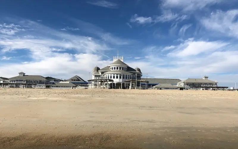 Hampton Beach shows a wide sandy shore with a large oceanfront pavilion under a blue sky.