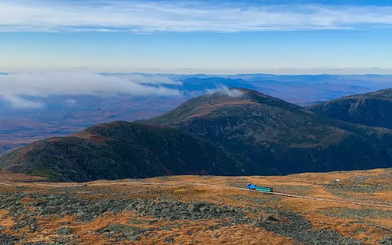 A scenic view of mountains near the Mount Washington Observatory with a train in the distance.