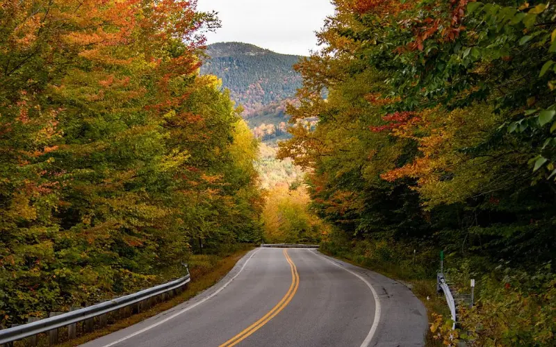 A winding road along the Kancamagus Highway is surrounded by colorful autumn trees.