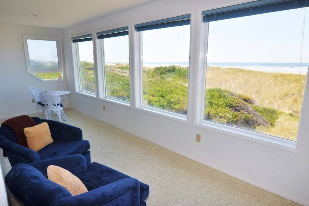 Sunlit beach house living room with large windows overlooking sand dunes and the ocean