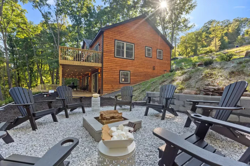 Outdoor stone fire pit with black Adirondack chairs on a gravel patio outside the Mad Men Lake House cabin