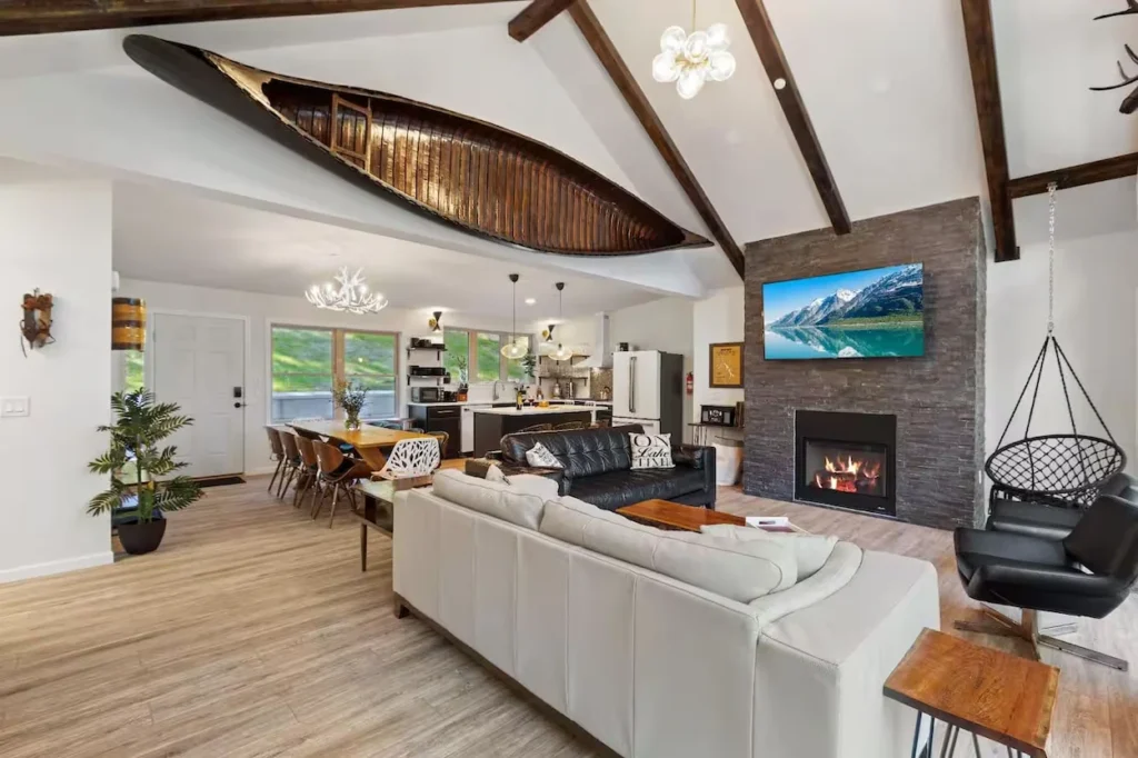 Cabin living room with a vintage canoe on a vaulted ceiling next to a stone fireplace