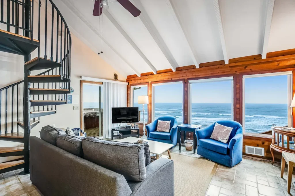 Beachfront cottage living room with a spiral staircase and large windows overlooking the ocean