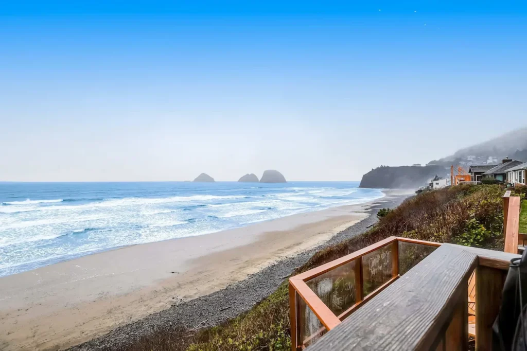 View of a sandy beach and ocean rock formations from a wooden cottage deck