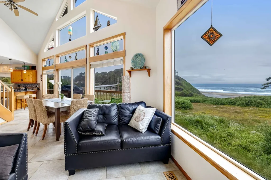 Beach house living room with a black leather loveseat next to a large window overlooking a grassy coast and ocean