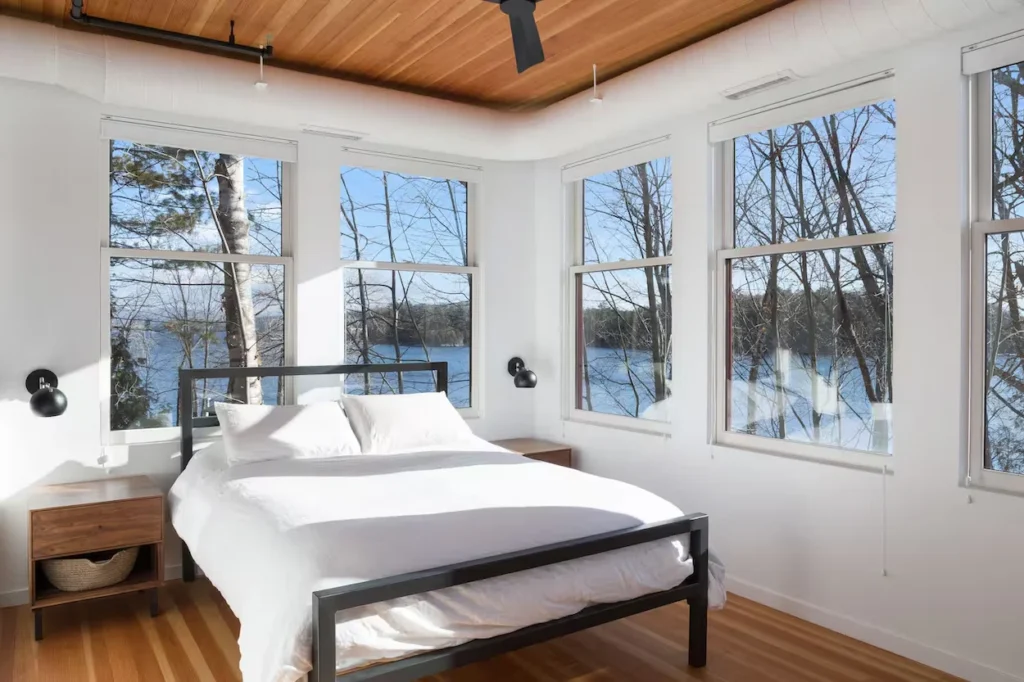 Modern bedroom with a white bed and large windows overlooking a lake