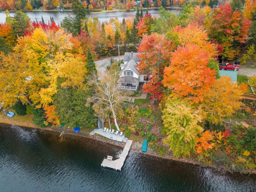 Aerial view of a lakefront house surrounded by colorful fall trees and a wooden dock