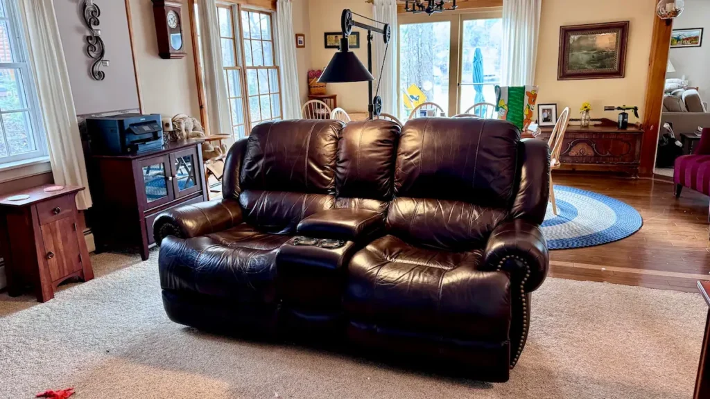 Dark brown leather reclining loveseat with a center console on a carpeted floor
