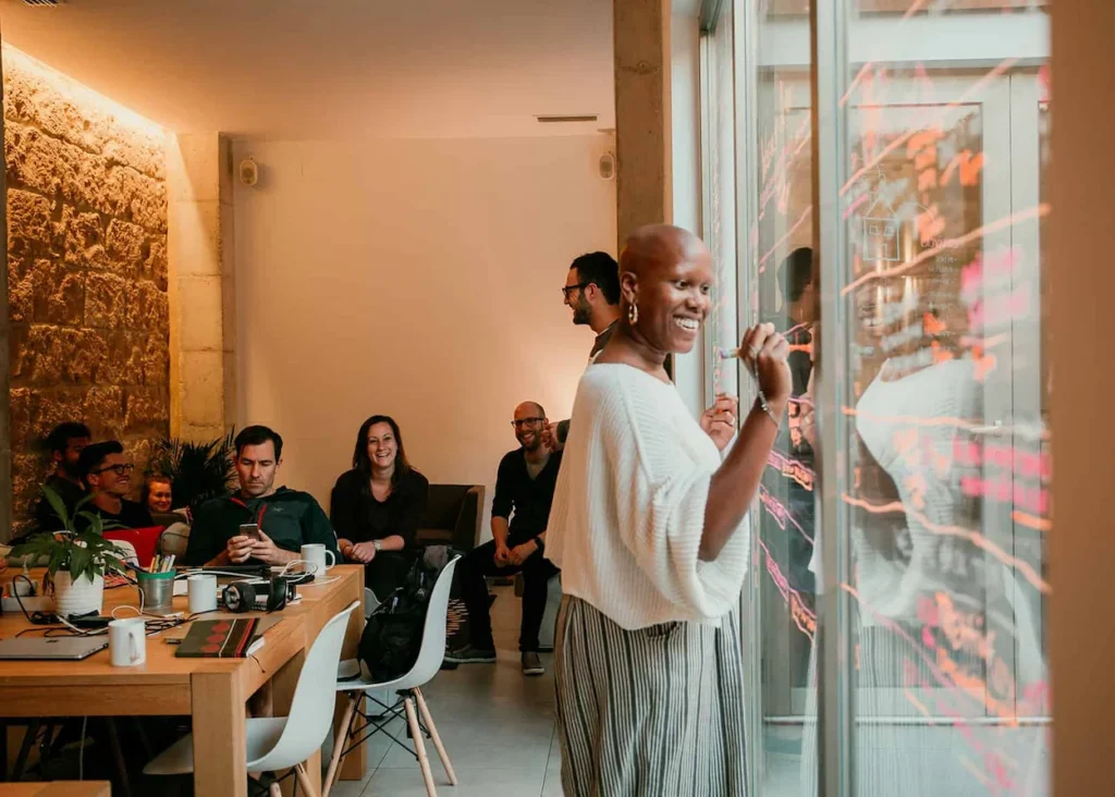 Woman writing on a glass wall while remote professionals watch inside the Sun and Co. coliving and coworking space in 2026