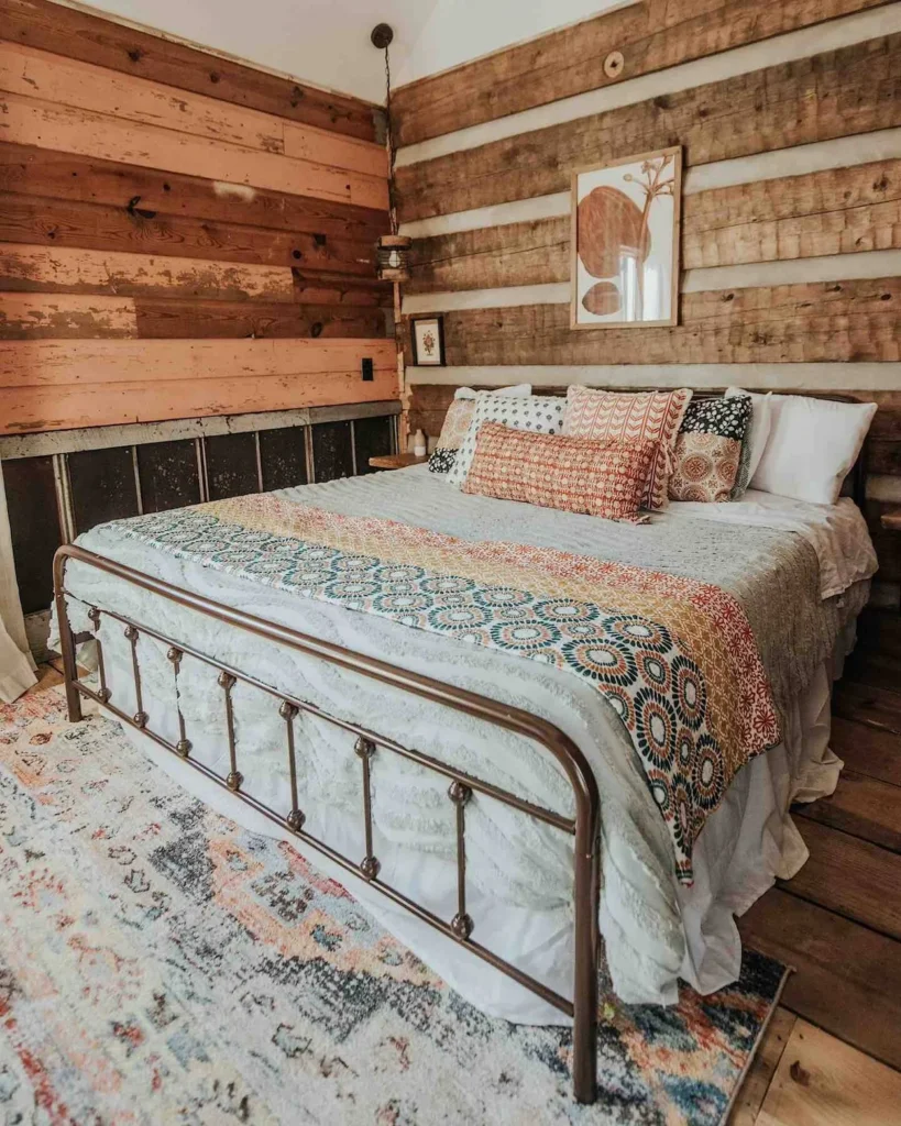 Log cabin bedroom with a metal frame bed, patterned bedding, and wooden walls