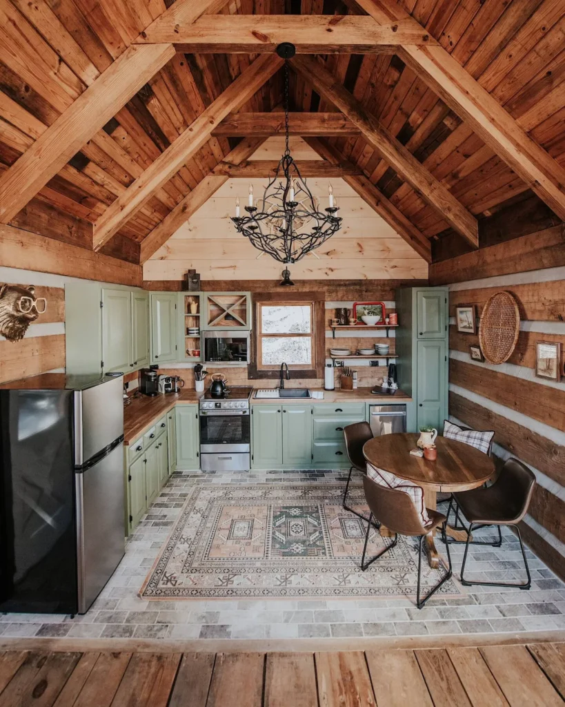 Rustic log cabin kitchen with sage green cabinets, brick tile flooring, and a round wooden dining table
