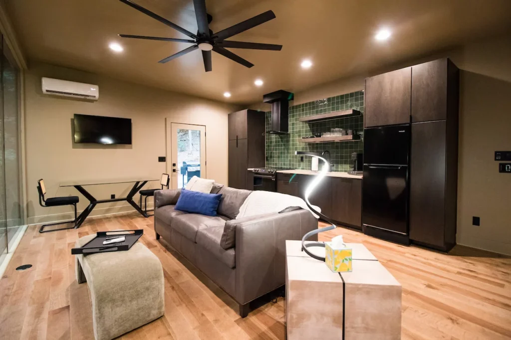 Modern open layout cabin interior with a gray sofa, green tile kitchen backsplash, and wood floors