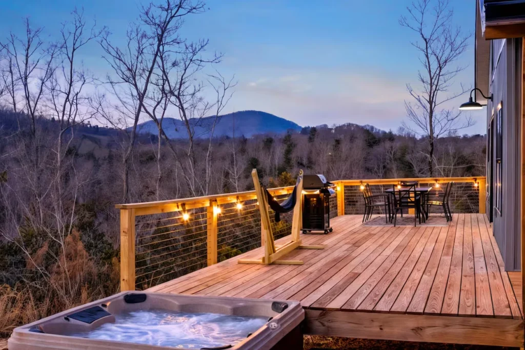 Wooden deck with a bubbling hot tub, hammock, grill, and dining set overlooking rolling mountains