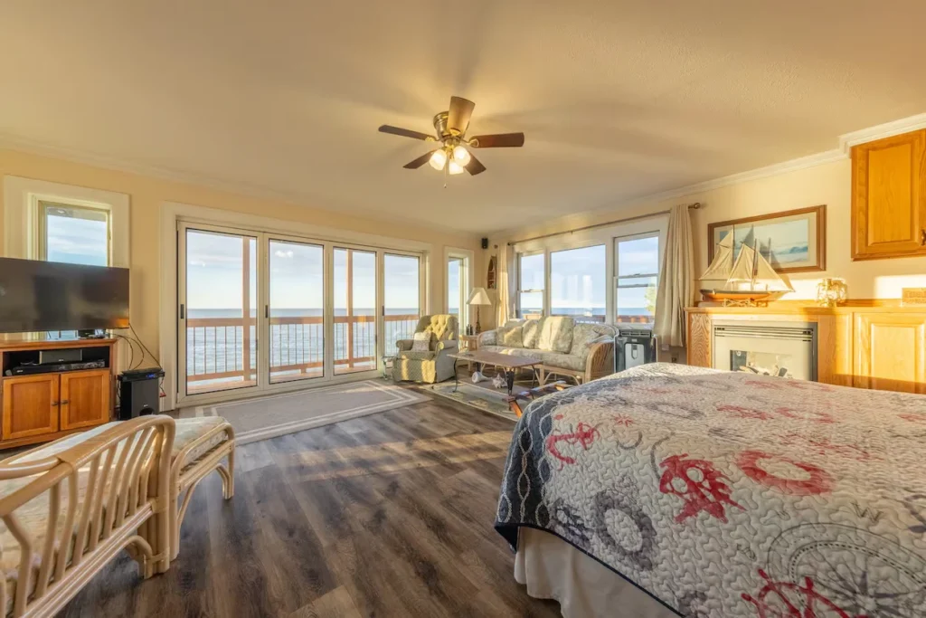 A bright lakefront bedroom and living combo with a nautical themed bed, glass patio doors, and a scenic water view