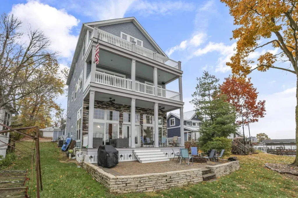 Three story blue vinyl siding vacation home with stacked covered balconies, a stone patio, and fall foliage trees