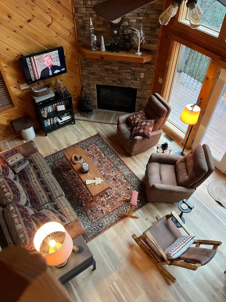 High-angle view of a cabin living room featuring an patterned rug, recliners, and a stone fireplace