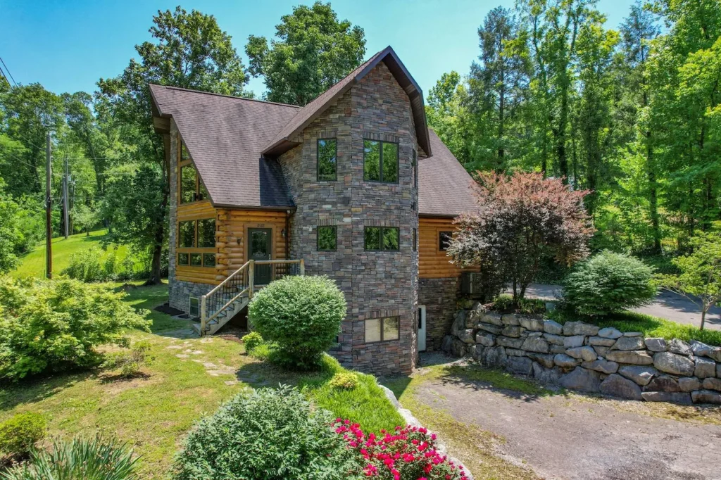 Large rustic luxury cabin with a distinct multi-story stone facade and log siding surrounded by green woods